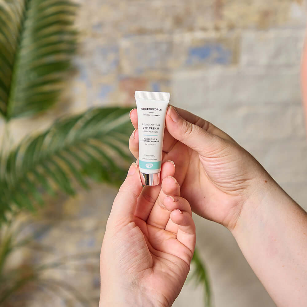 Person holding Green People Rejuvenating Eye Cream with firming and toning formula, against a soft background with green leaves.
