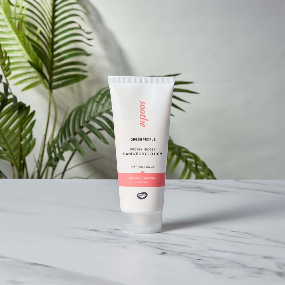 Green People Protein-Boost Hand and Body Lotion with quinoa and calendula, displayed on marble with green leaves in the background.