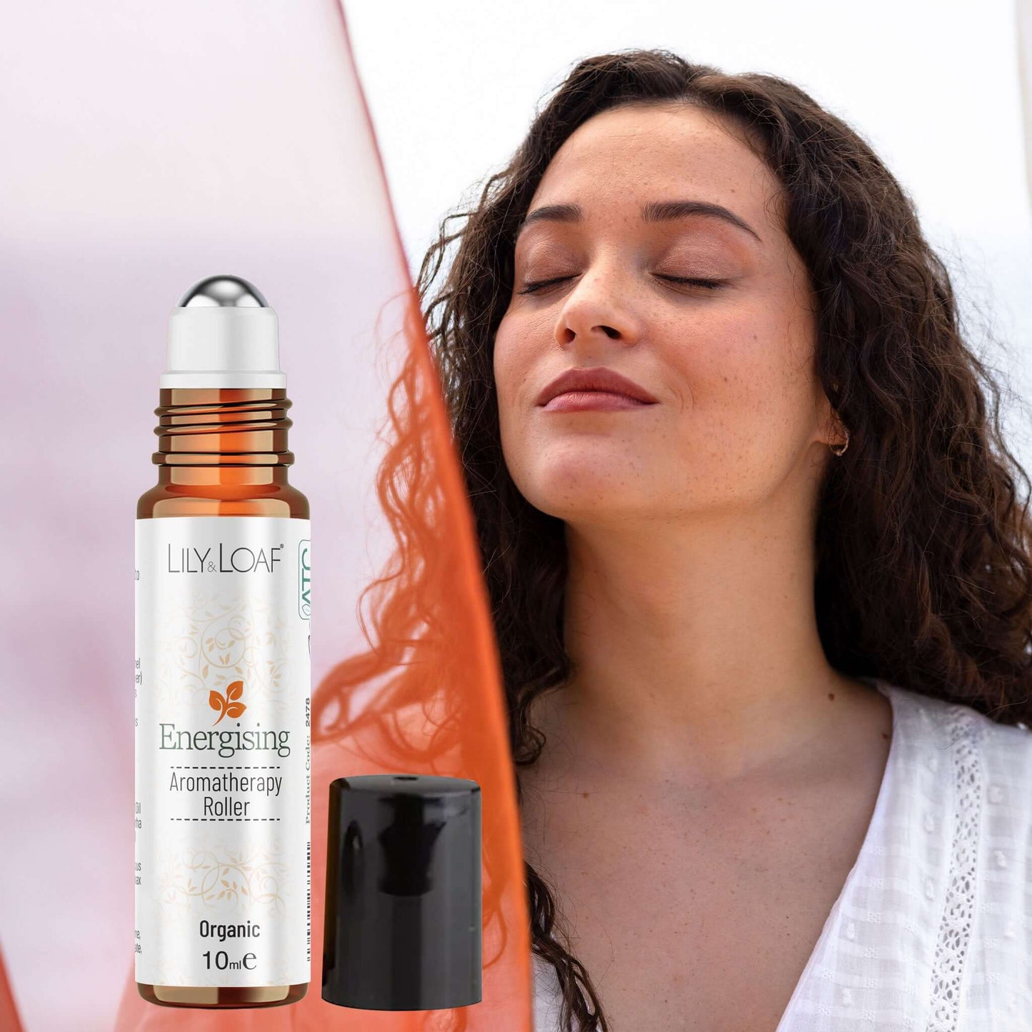 Woman with eyes closed next to a Lily & Loaf Energising aromatherapy roller bottle on a white background