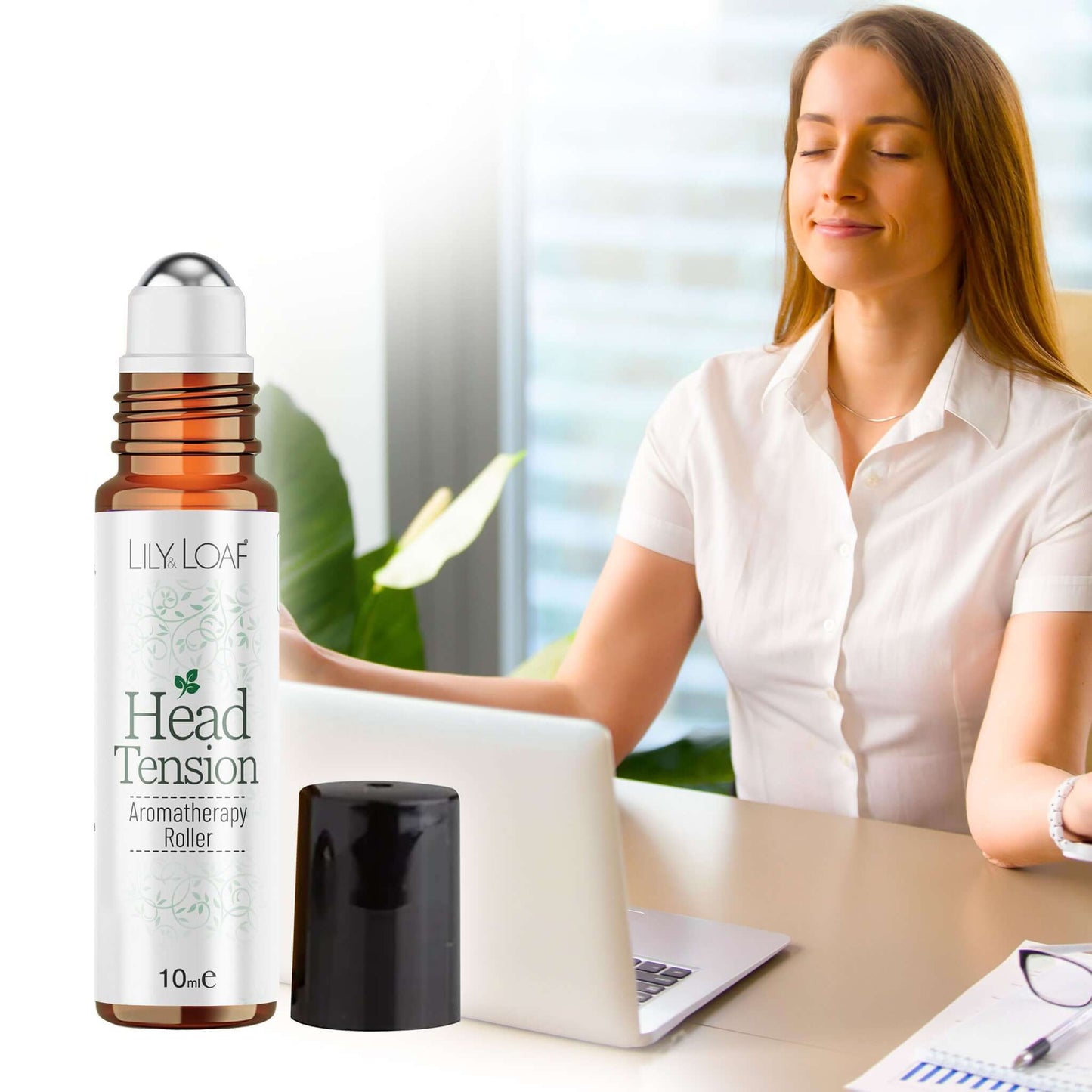 Woman sitting at a desk with a laptop, using a 'Head Tension' roller bottle by Lily & Loaf.