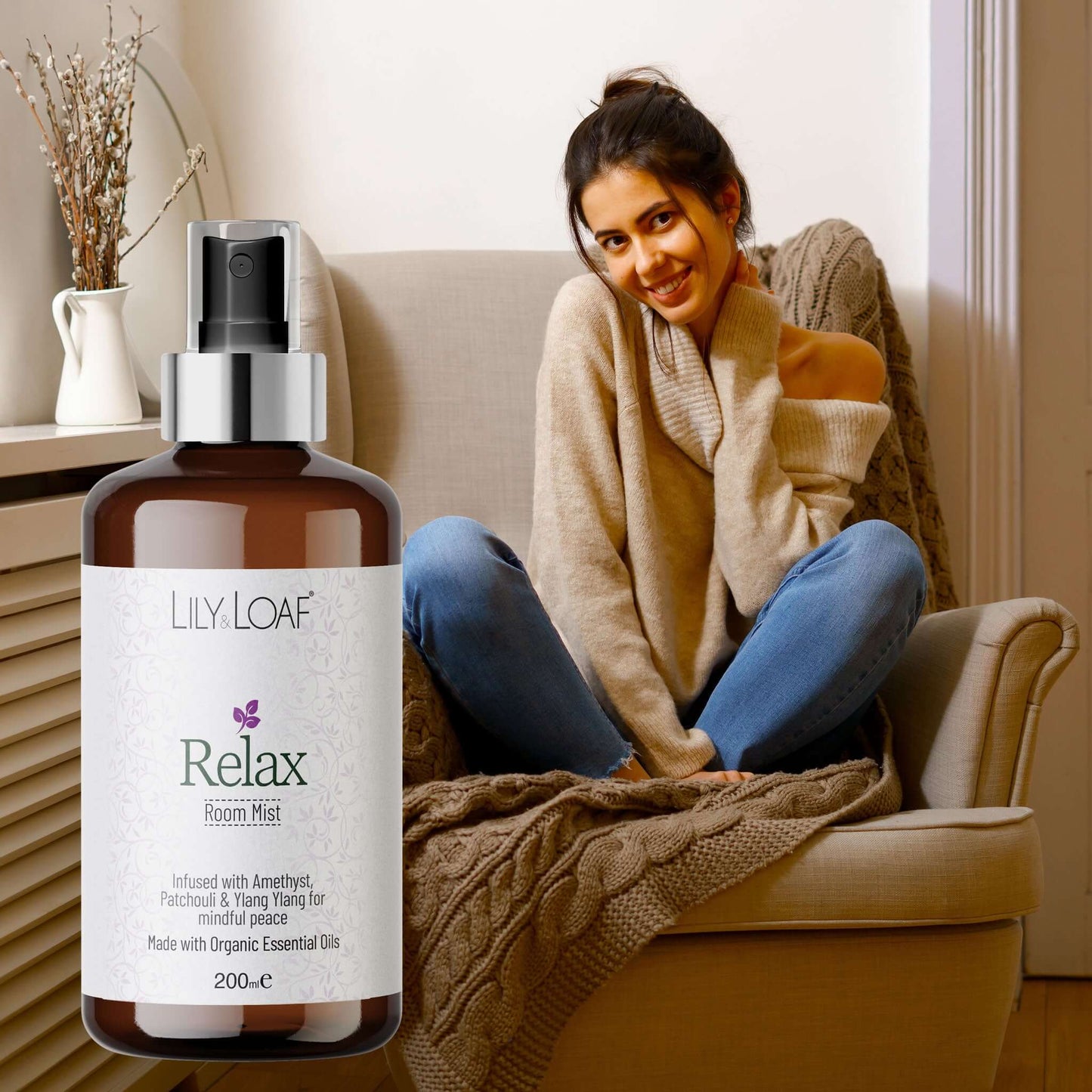 Bottle of Lily & Loaf Relax Room Mist with a woman sitting on a couch in the background
