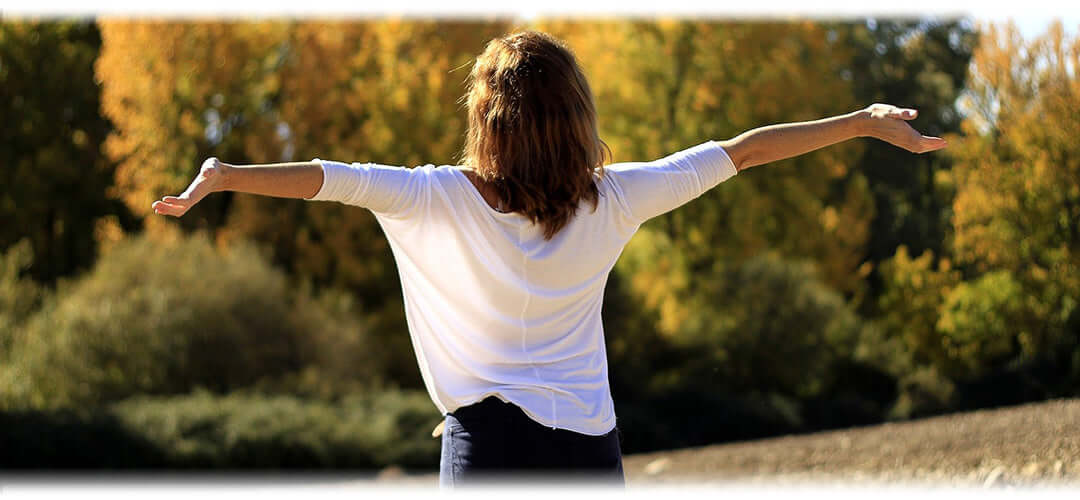 A woman standing outdoors surrounded by trees and greenery, enjoying nature.