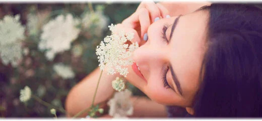 A woman standing in a meadow of flowers. The image suggests the topic of essential oils and their uses.