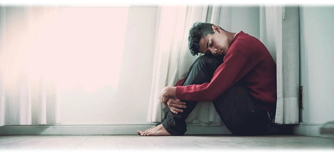 A man sitting curled up and anxious on the floor