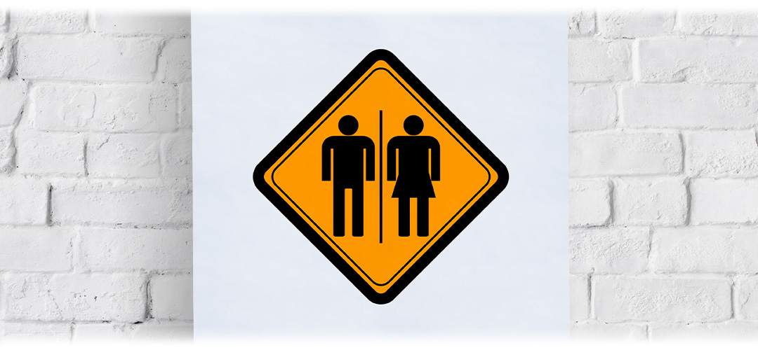 Yellow and black unisex bathroom sign with male and female icons on a white brick wall background.