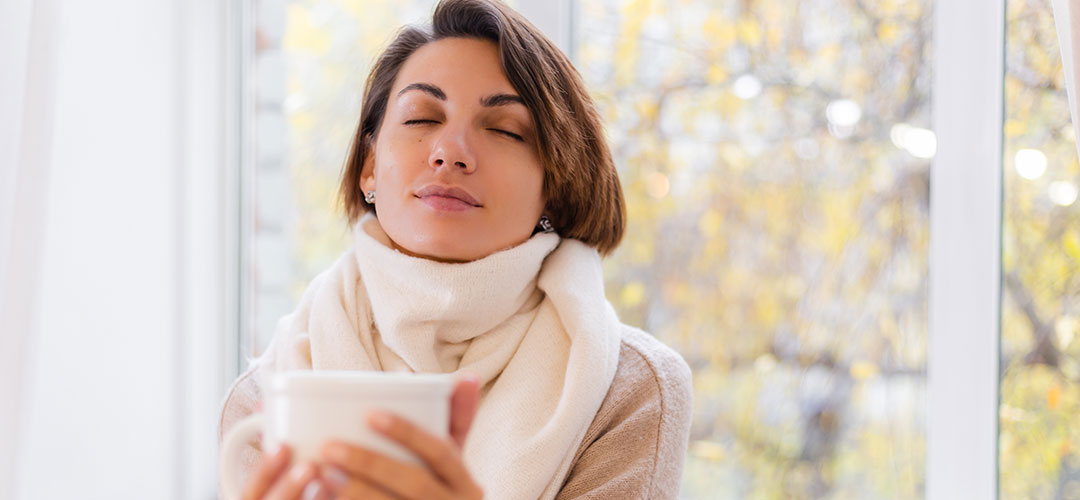 warm-portrait-woman-sitting-windowsill-with-cup-hot-tea-coffee-wearing-sweater-white-scarf