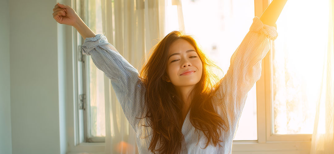woman-stretching-happily-on-bed-in-bright-sunlight