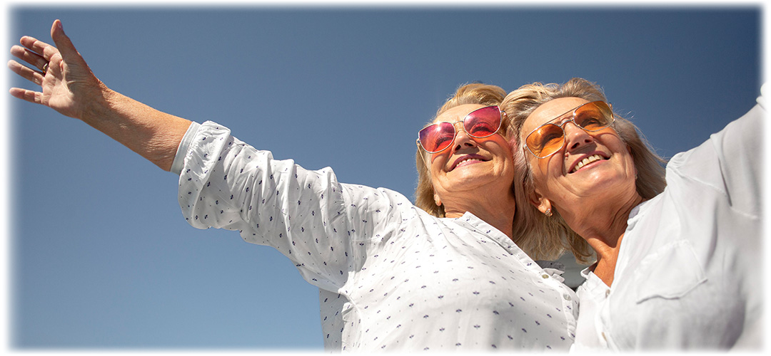 Two women wearing bright coloured sunglasses smiling in the sunshine