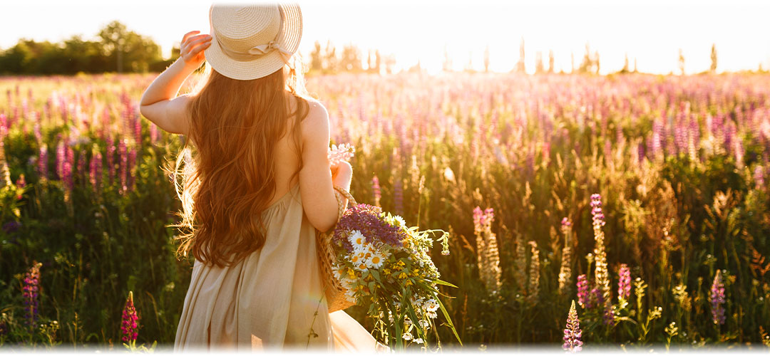 A woman in a straw hat walking through a field of flowers