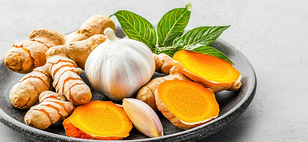 fresh-turmeric-root-slices-and-whole-garlic-on-black-plate