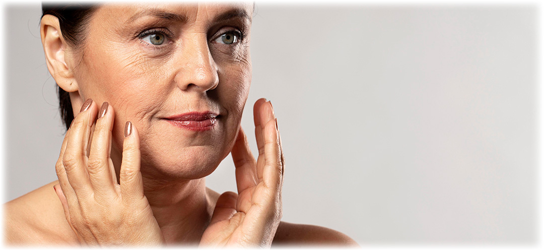 Mature woman touching her face with both hands, showcasing healthy skin and natural beauty on a neutral background