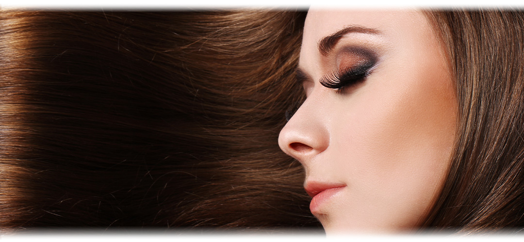 A close-up image of a woman with shiny, healthy hair, illuminated by light. The image depicts the concept of hair care and achieving shiny, lustrous hair