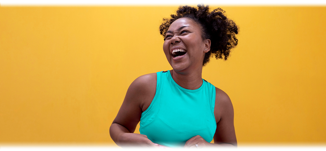 Joyful woman in a teal tank top laughing against a bright yellow background.