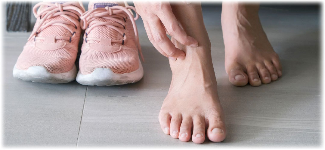 A person massaging their sore foot beside a pair of pink athletic shoes. This emphasizes the need for proper foot care and comfort after physical activity, highlighting the benefit of using Lily & Loaf products