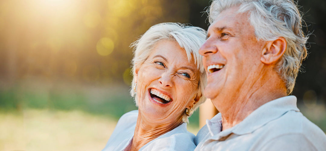 middle age couple laughing on a bench in the sunshine
