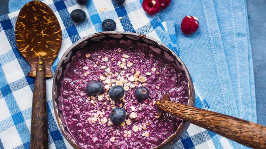 Purple blueberry porridge topped with berries in a breakfast bowl.