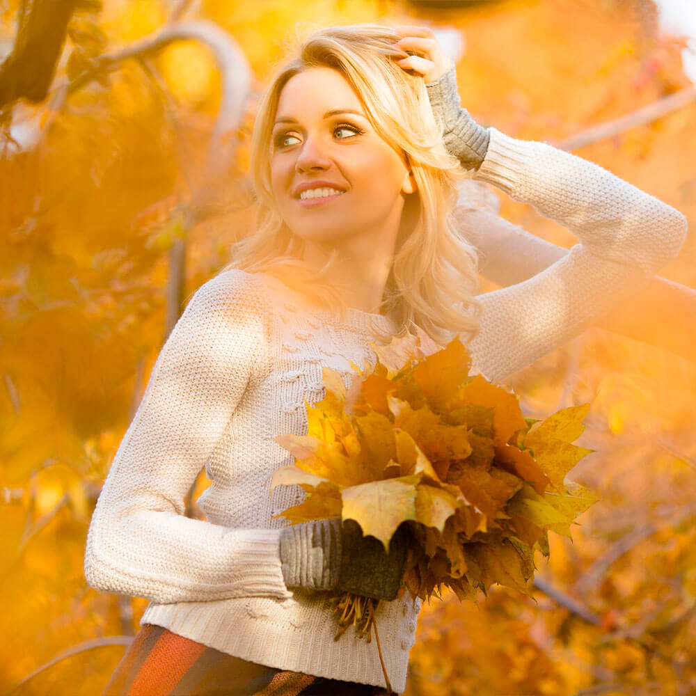 Woman holding autumn leaves in a forest with orange foliage