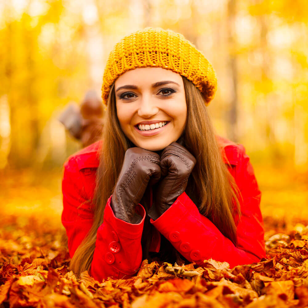 Woman in a red coat and yellow beanie lying on autumn leaves