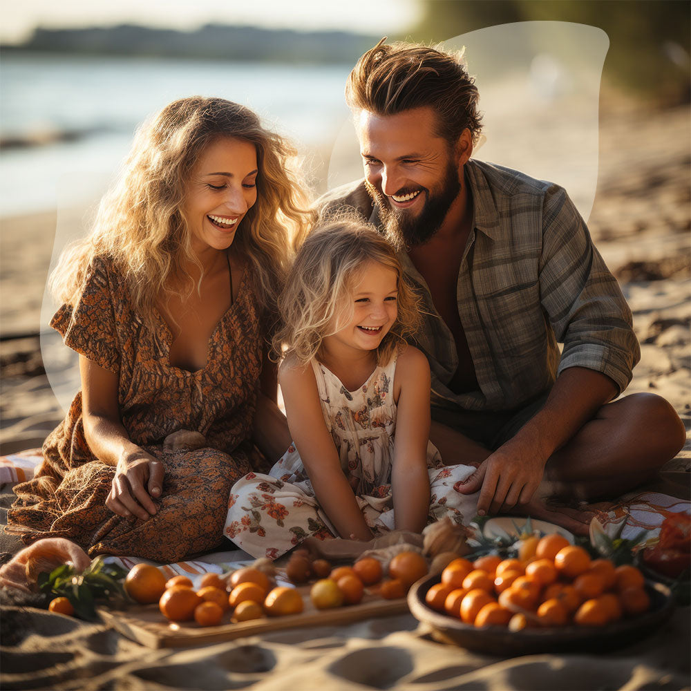 Family of three sitting on a beach with a picnic spread, smiling and enjoying their time together.