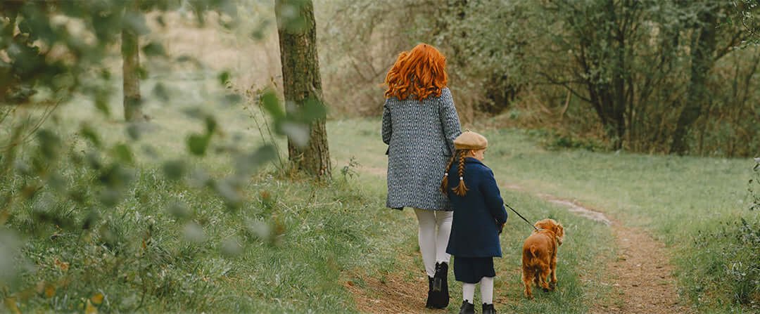 A lady and little girl with red hair taking their red haired dog for a walk in the woods.