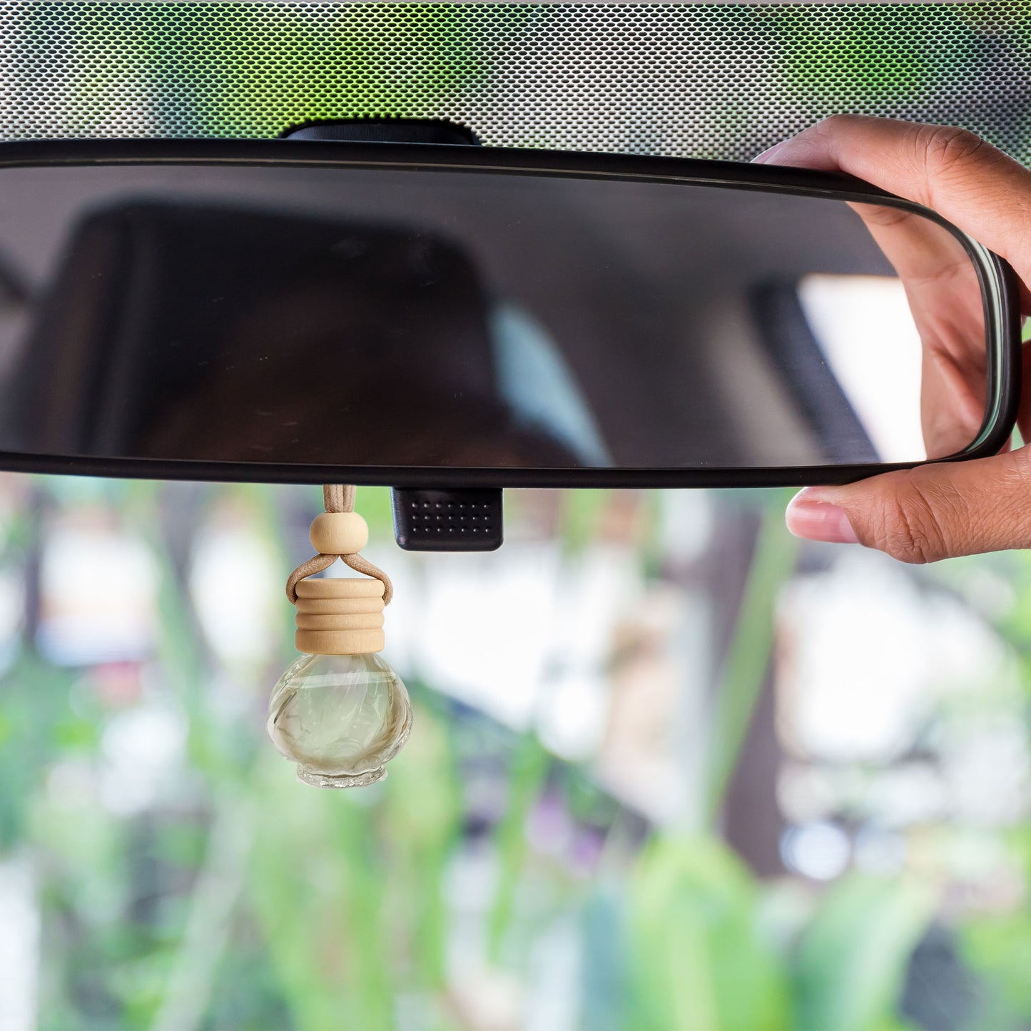 Car rear view mirror with a decorative air freshener hanging from it, against a blurred outdoor background.