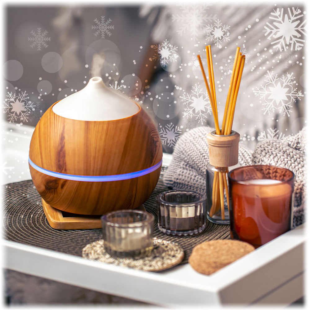 Wooden diffuser with a candle and reed diffuser on a decorative surface with snowflake decorations.