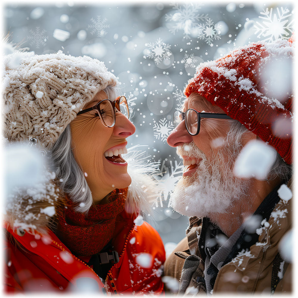 Two people in winter clothing laughing together with snowflakes falling around them.