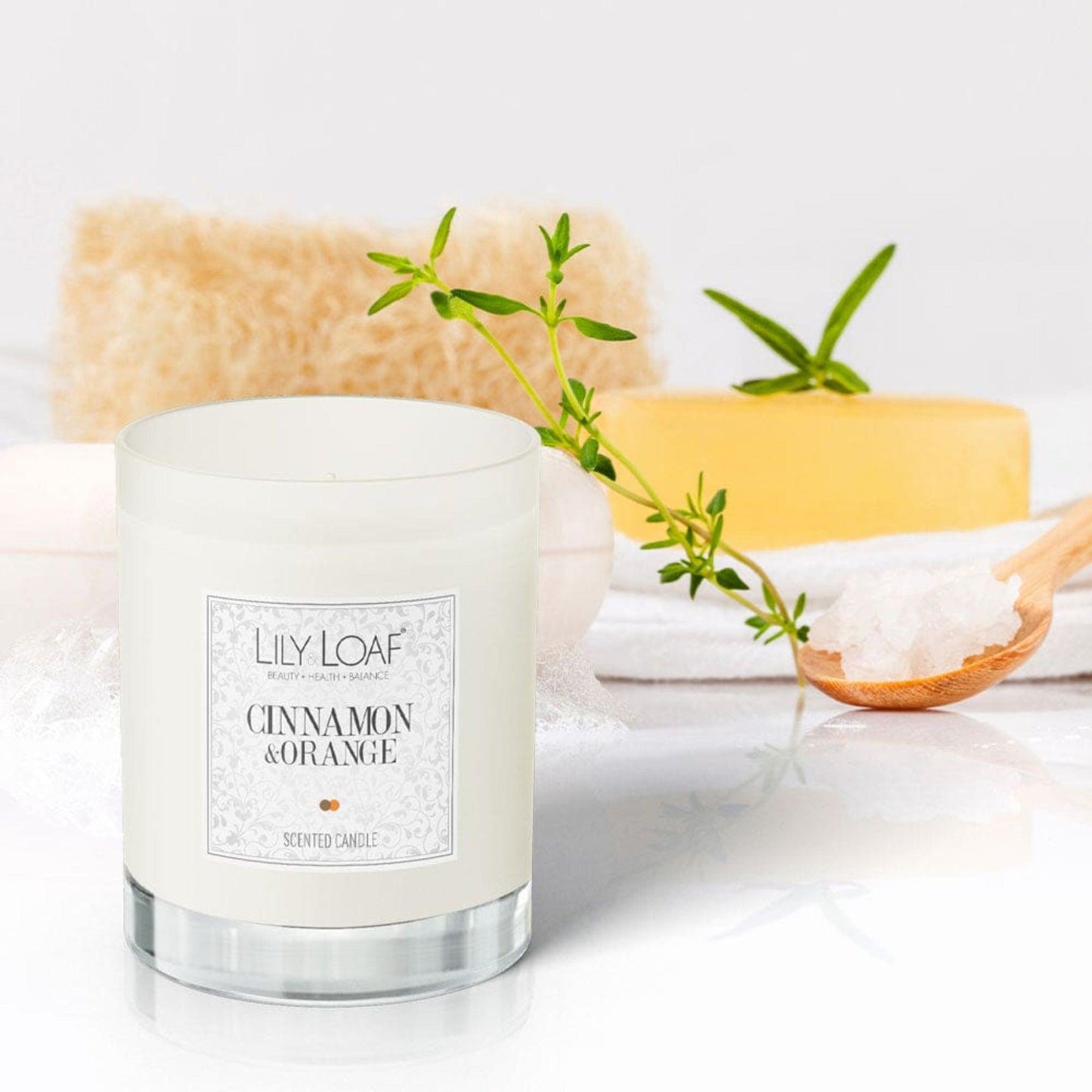 Lily & Loaf Cinnamon and Orange Soy Wax Candle on a bathroom counter surrounded by soap, bath salts and a loofah