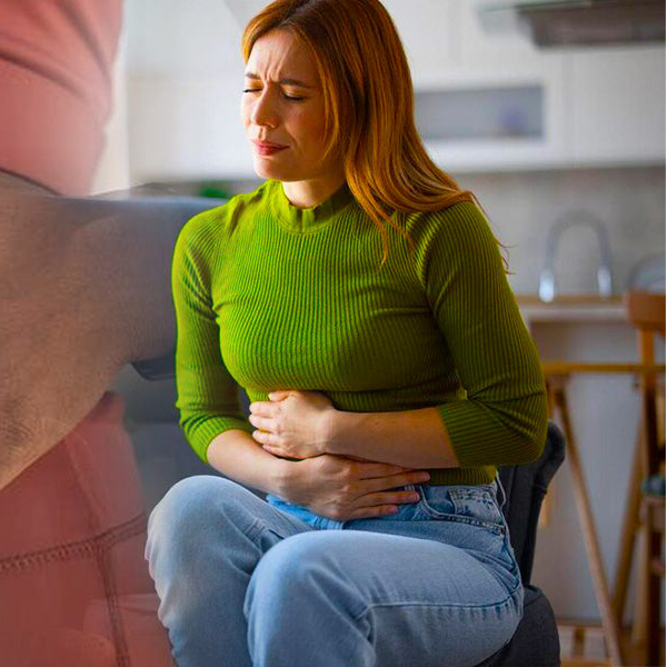 Woman in green sweater holding her stomach in a kitchen setting