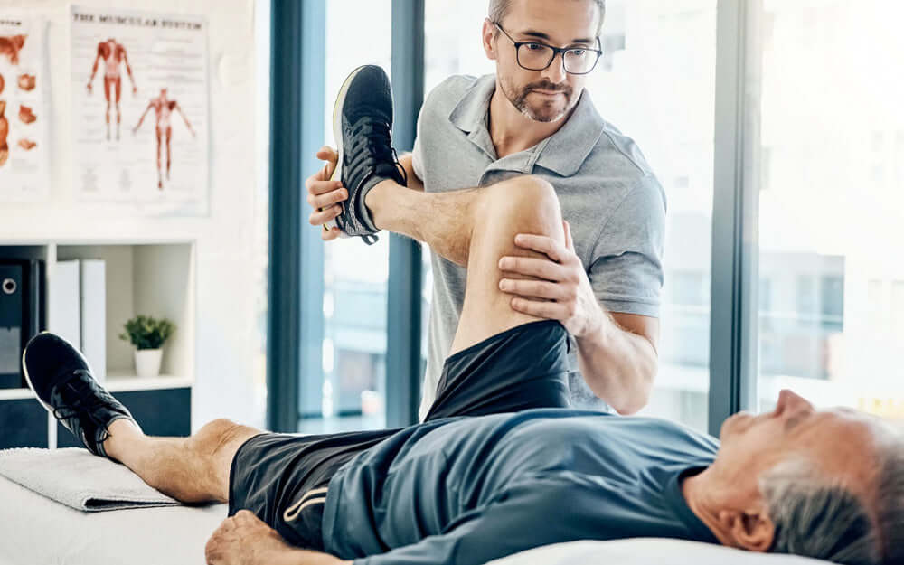 Physical therapist assisting a male leg and knee joint