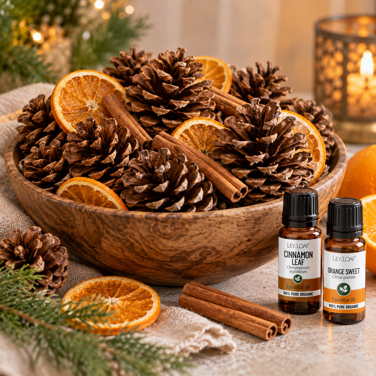 A styled holiday still life featuring amber glass essential oil bottles, cinnamon sticks, star anise, dried orange slices, pinecones, and evergreen branches arranged in a wooden bowl on a warm wooden table with soft candlelight in the background.
