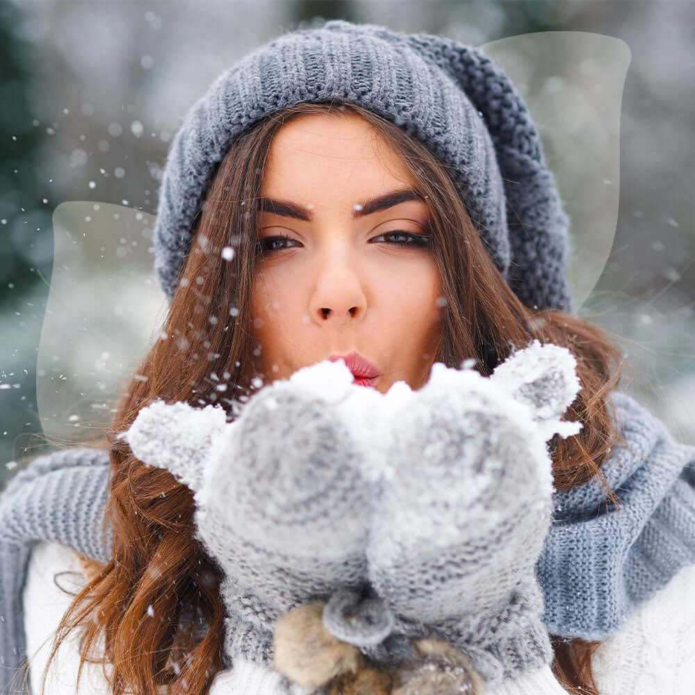Woman blowing snowflakes in a snowy setting indicating Immune Support