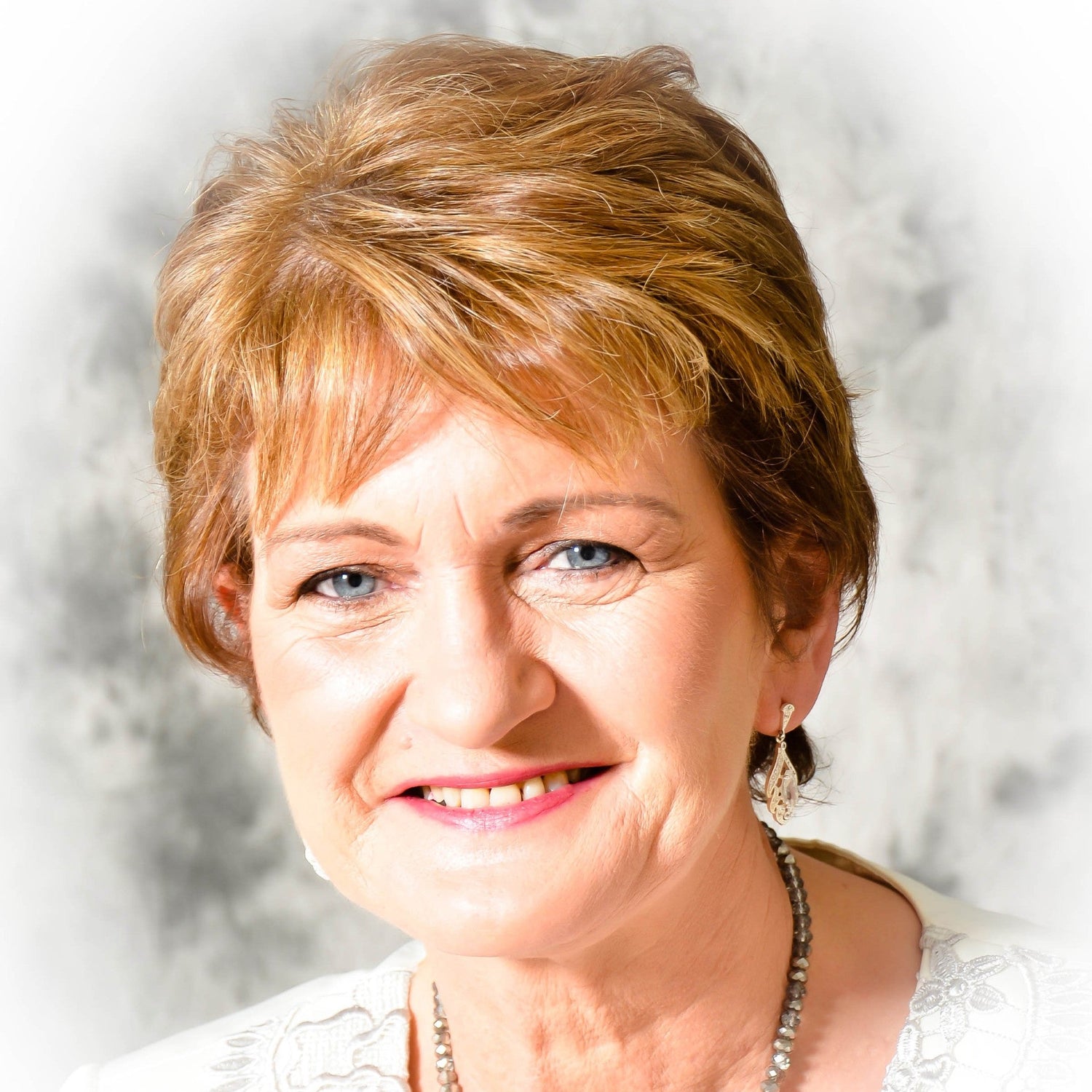 Woman with short blonde hair wearing a white top and necklace against a light background