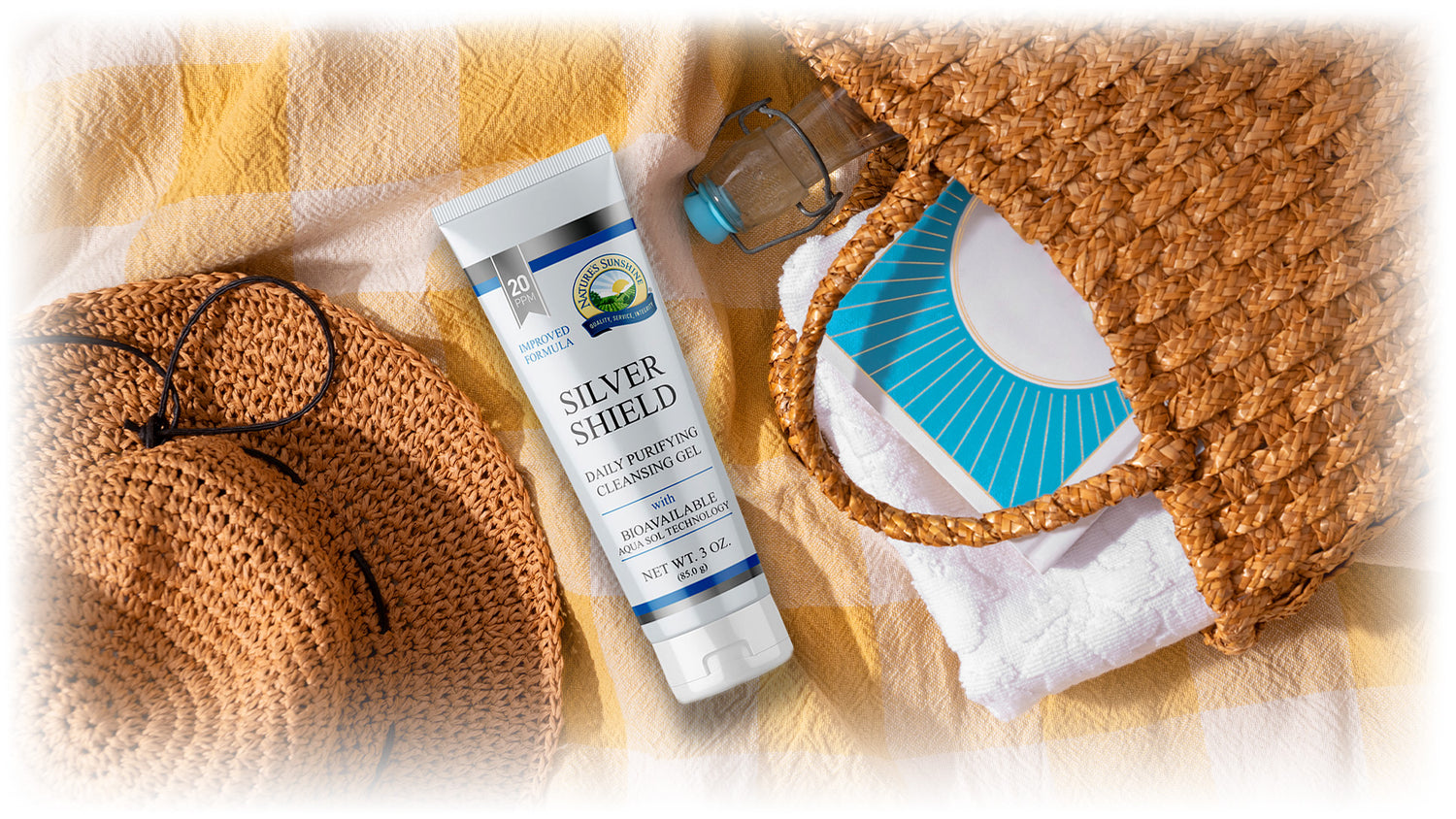 A tube of Silver Shield Gel next to a woven wicker hat and beach bag
