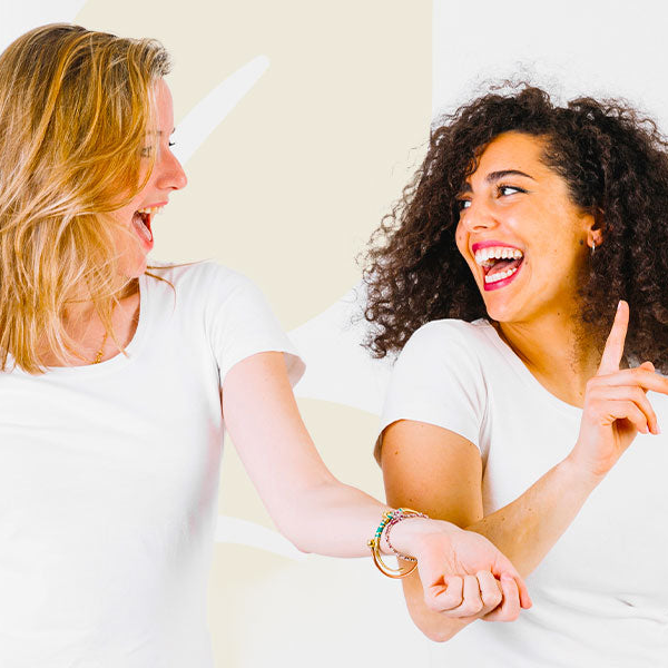 Two women laughing and interacting with each other against a plain background