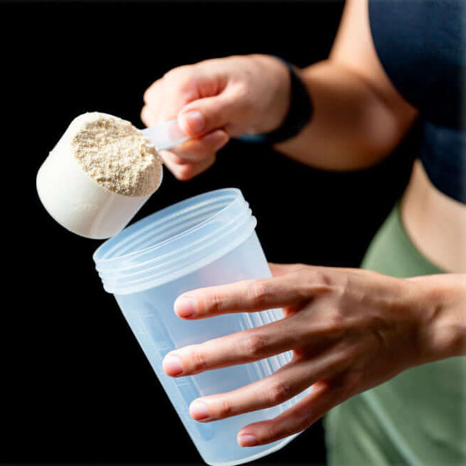 Person preparing a protein shake with Lily & Loaf powder, supporting active and healthy lifestyles.