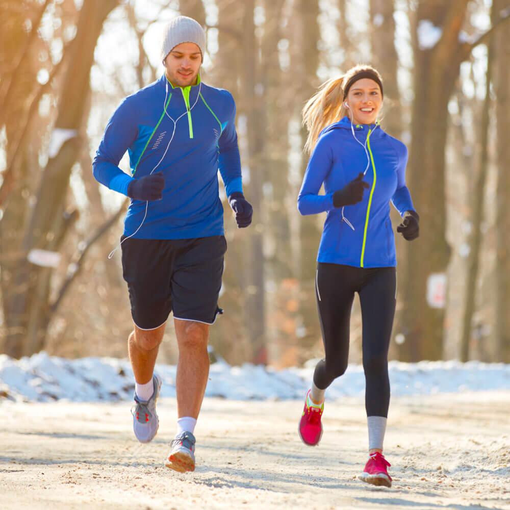 A man and woman in matching blue sportswear jogging on a snowy Winter day