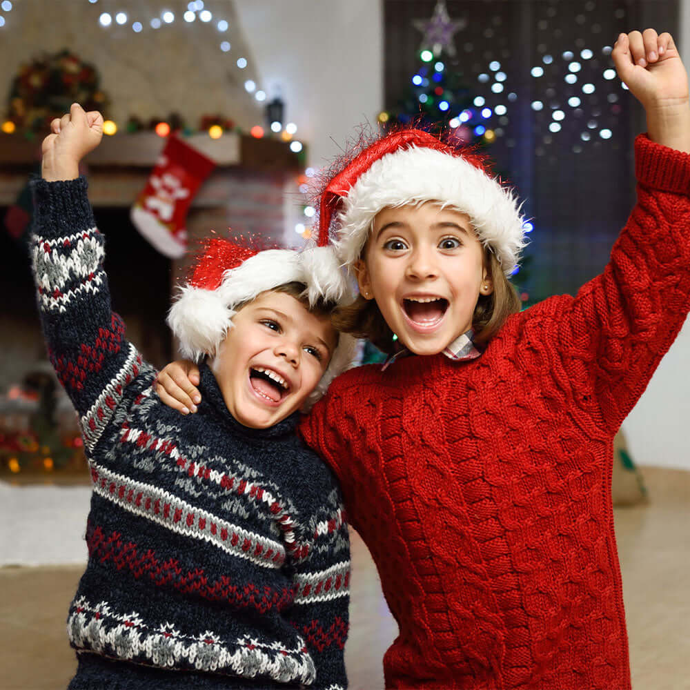 A boy and girl in Christmas jumpers and Santa hats cheering and happy