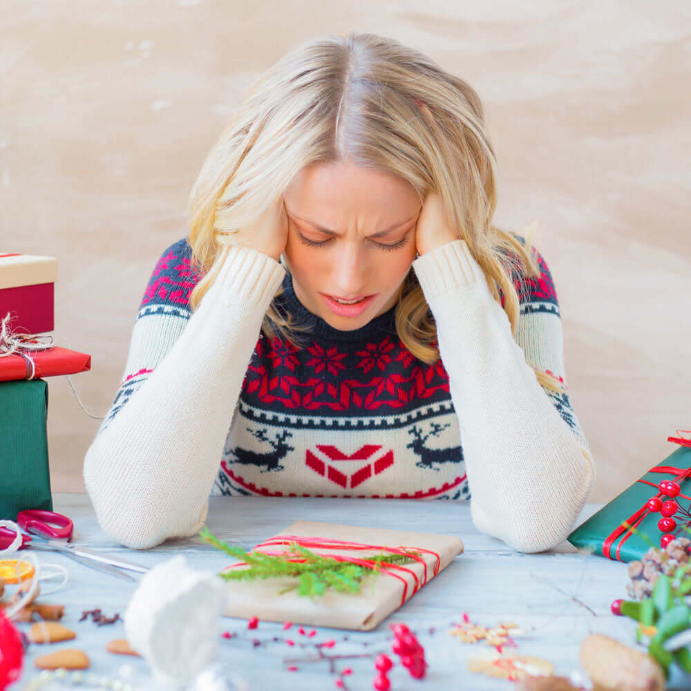 A stressed looking woman in a Christmas jumper wrapping presents