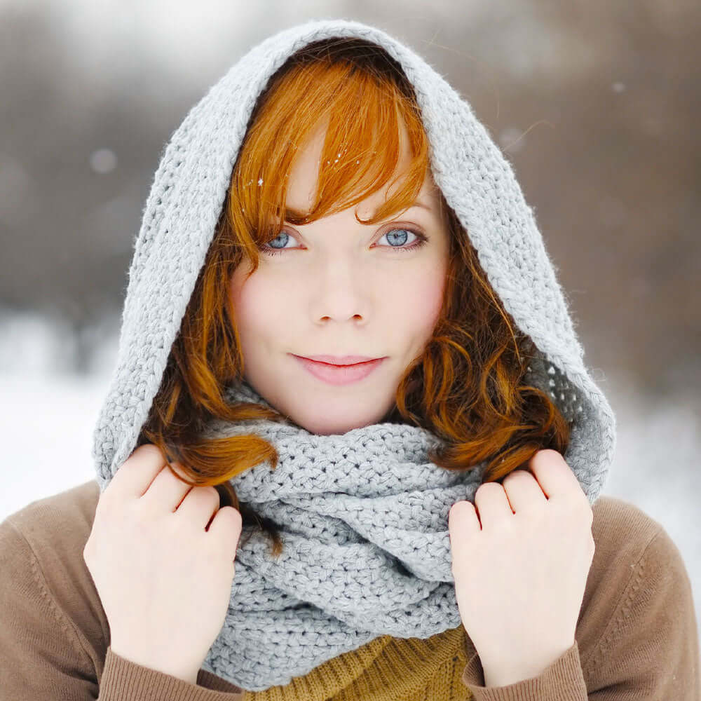 A redhead woman wearing a grey scarf over her head to protect herself from snowfall