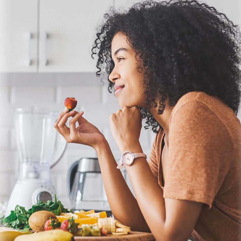 A woman eating a strawberry from a selection of fruits on a chopping board