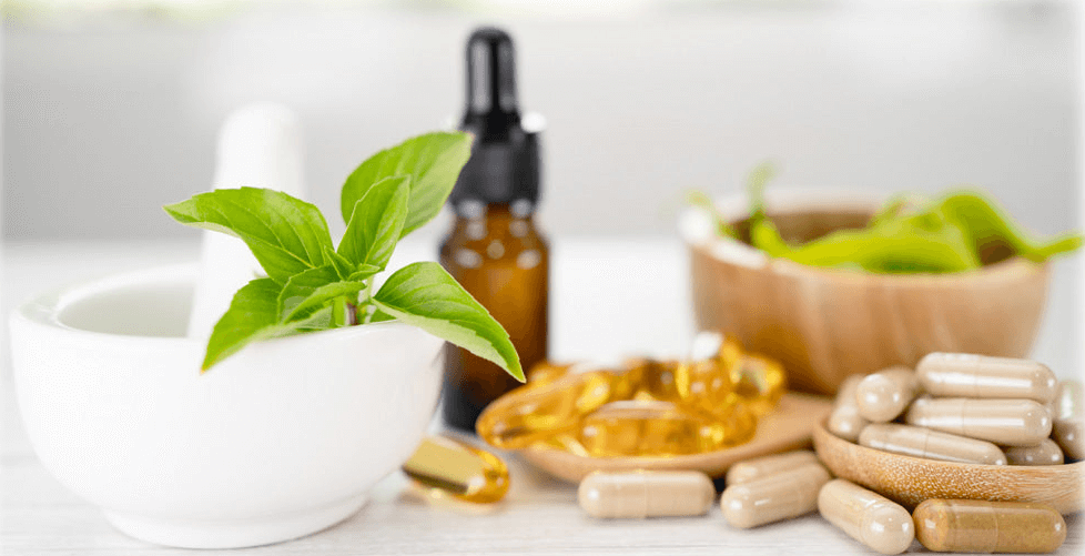 A selection of capsules in wooden bowls next to an amber dropper bottle and white pestle and mortar