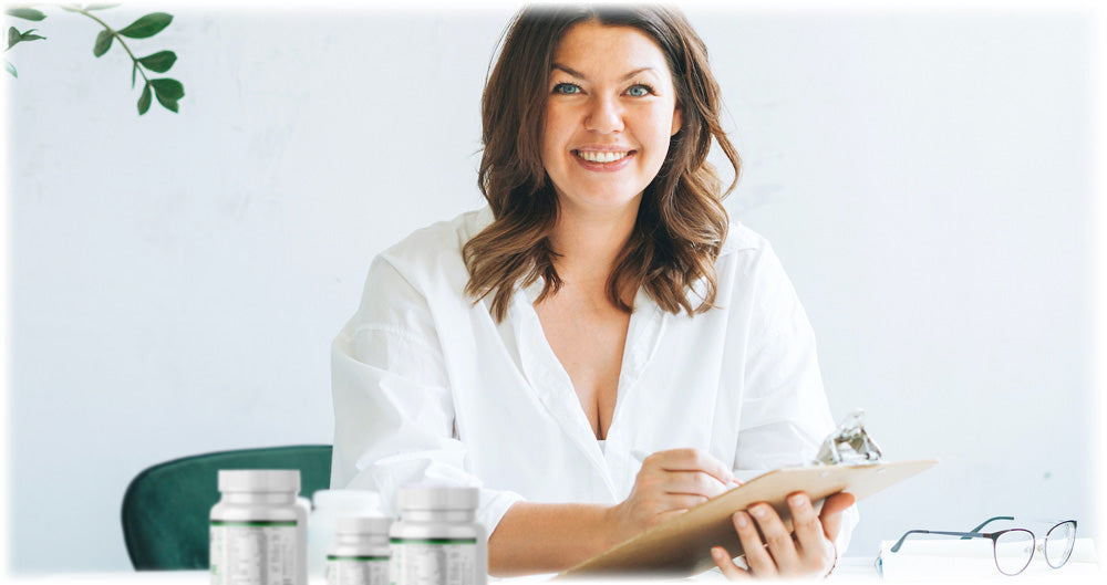 Smiling woman holding a clipboard, sitting at a desk with supplement bottles, representing health consultation and personalized wellness planning.