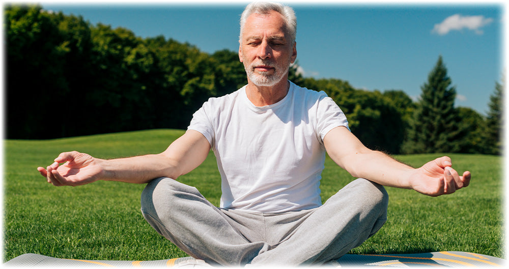 Older man meditating outdoors on a sunny day, sitting cross-legged on a mat in a peaceful park, promoting mindfulness and relaxation.