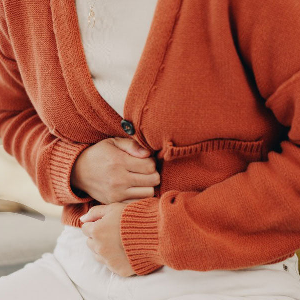 Close-up of a person wearing an orange cardigan with their hands clasped together.