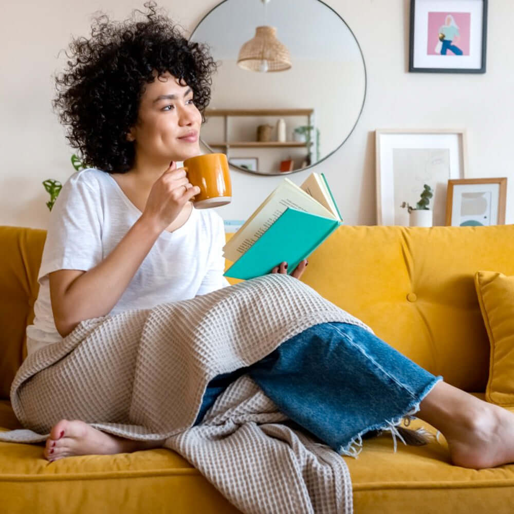 A woman relaxing with a cup of tea on a yellow sofa