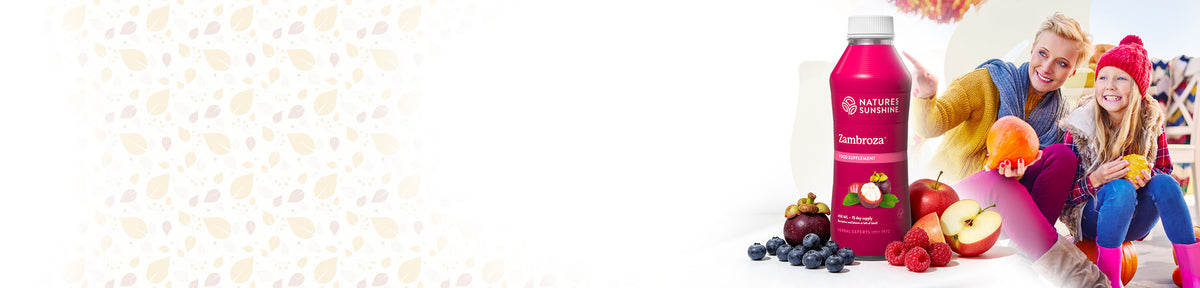 Nature's Sunshine Zambroza bottle shown on the right side of a wide white banner, with fruit pieces around it and two smiling people in a bright outdoor setting on the right edge.