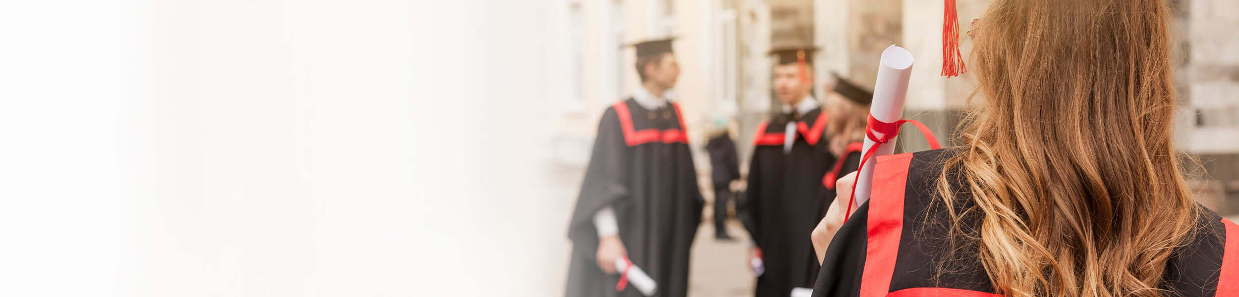 Graduates in caps and gowns celebrating outdoors, with one woman holding a diploma in the foreground.