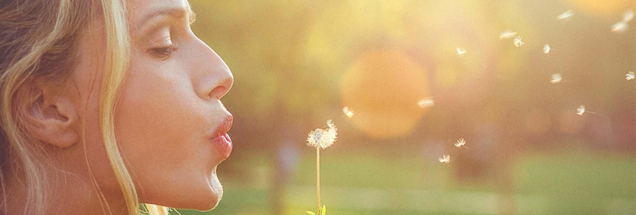 A woman blowing the seeds off a dandelion