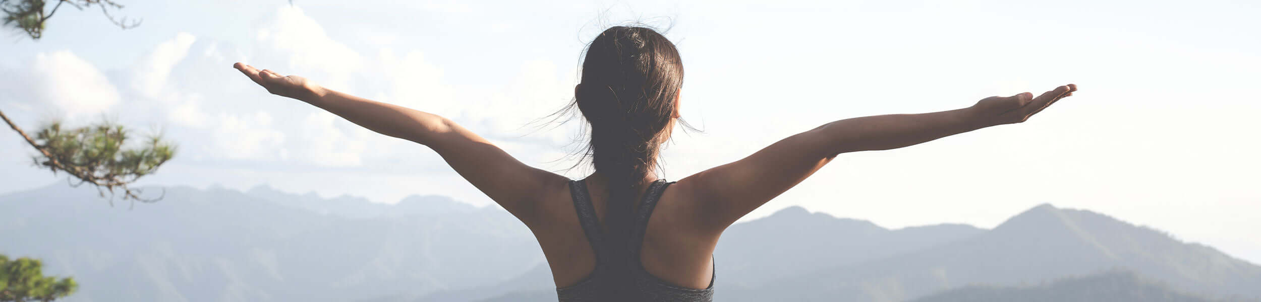 A woman stood with her arms outstretched looking at a mountain range in the distance